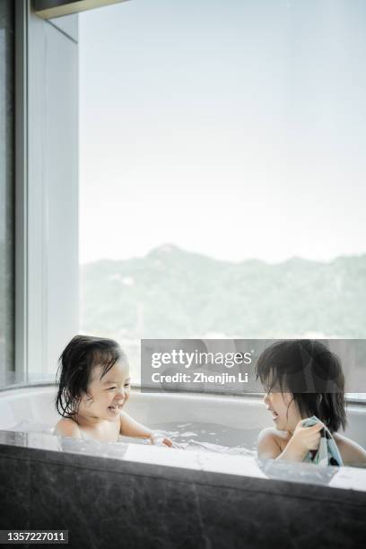 2 years twin sisters taking a bath in a bathtub by the window - girls modern room stock-fotos und bilder