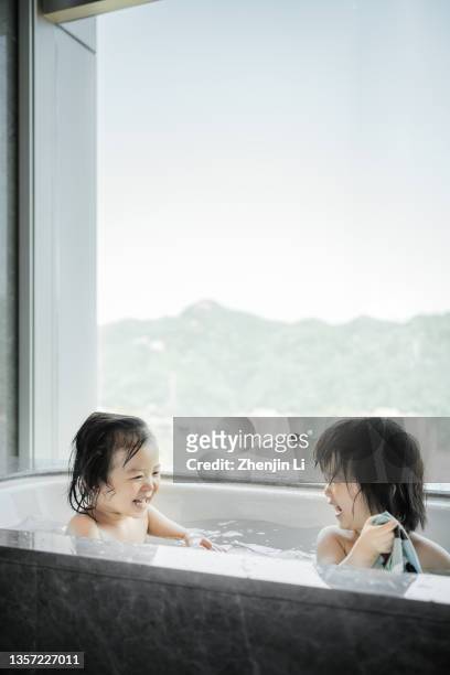 2 years twin sisters taking a bath in a bathtub by the window - modern baby nursery stock pictures, royalty-free photos & images