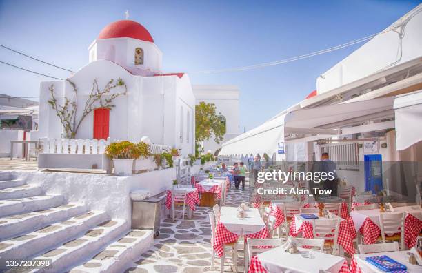 tables in a tavern in front of typical red top church in mykonos town, cyclades, greece - mediterranean-blue-roof-santorini stock pictures, royalty-free photos & images