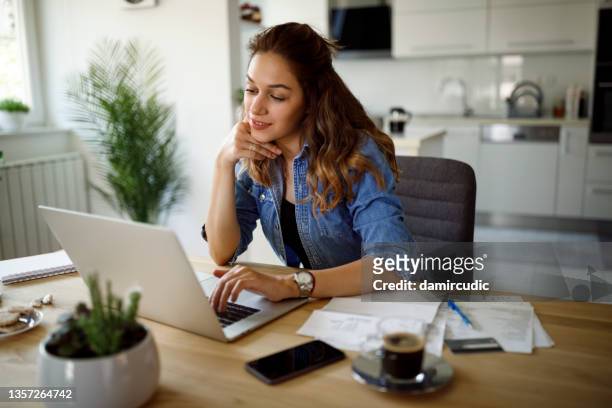 smiling young woman working at home - investment research stock pictures, royalty-free photos & images