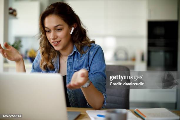 jovem sorridente com fones de ouvido tendo chamada de vídeo no computador portátil em casa - video conference - fotografias e filmes do acervo