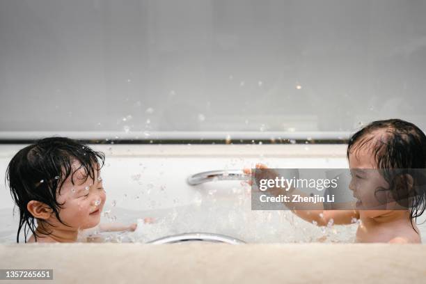 young sisters splashing water in a bathtub - asian water splash stock pictures, royalty-free photos & images