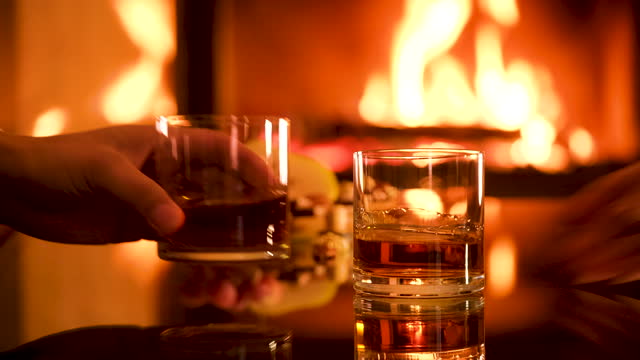 Young couple has romantic dinner with whiskey over fireplace background.