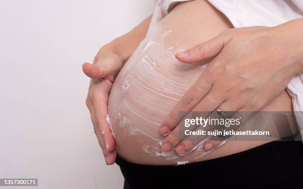 happy pregnant woman apply skincare cream lotion on pregnant belly to prevent stretch mark. healthy skin massage treatment and moisture care concept - estrias fotografías e imágenes de stock