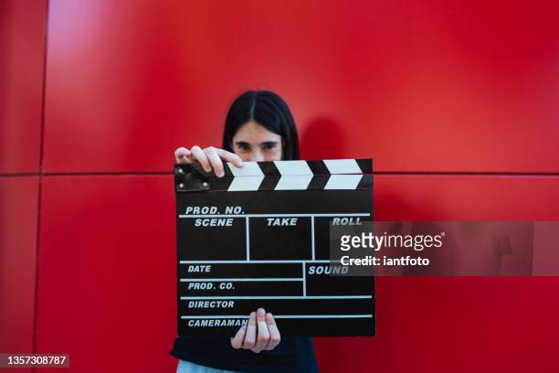 una ragazza che tiene un assicella di film davanti a uno sfondo rosso. concetto di regista cinematografico. - film director foto e immagini stock