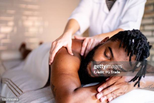 hombre adulto medio recibiendo masaje en los hombros en un spa - black massage therapist fotografías e imágenes de stock