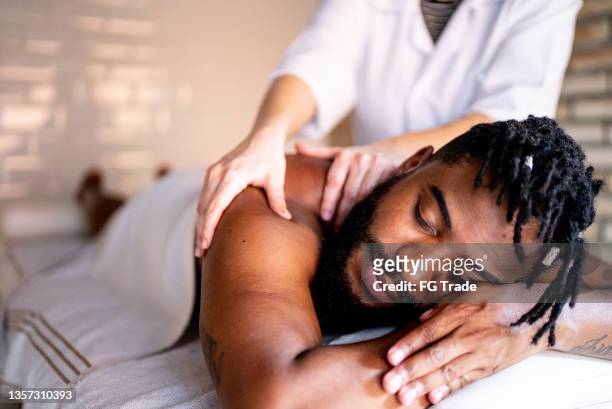 mid adult man receiving massage on shoulders at a spa - african ethnicity spa stock pictures, royalty-free photos & images