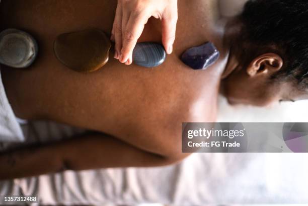 terapeuta poniendo piedras calientes en la espalda de la mujer en un spa - black massage therapist fotografías e imágenes de stock