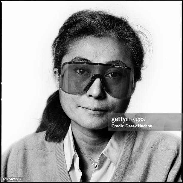 Portrait of Japanese multimedia artist and musician Yoko Ono, in a pair of Porsche-brand, wrap-around sunglasses, as she poses in her apartment at...