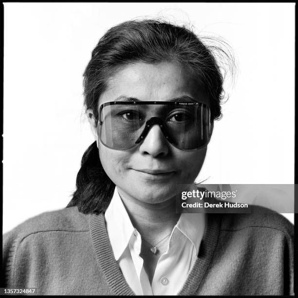 Portrait of Japanese multimedia artist and musician Yoko Ono, in a pair of Porsche-brand, wrap-around sunglasses, as she poses in her apartment at...