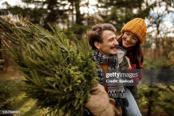 young man carrying girlfriend and christmas tree home on sunny winter day - christmas gift bag stock pictures, royalty-free photos & images