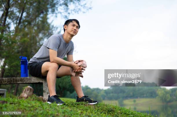 junger asiatischer mann entspannt sich nach dem training in einem öffentlichen park - bank müde frühling stock-fotos und bilder