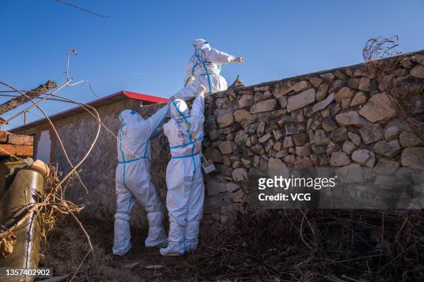 The police assist a nurse to climb onto a wall for collecting swabs from villagers under isolation for the COVID-19 nucleic acid test at Hongchang...
