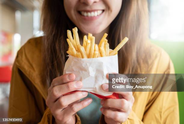 close up of young asian woman holding a french fries before eating. - frites stockfoto's en -beelden