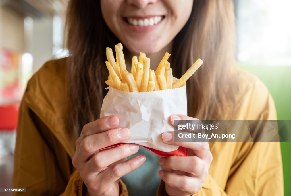 Close up of young Asian woman holding a french fries before eating.