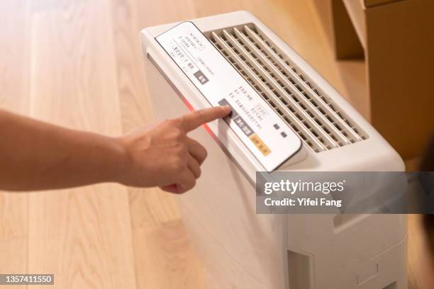 woman adjusting air purifier at home - luftfilter stock-fotos und bilder
