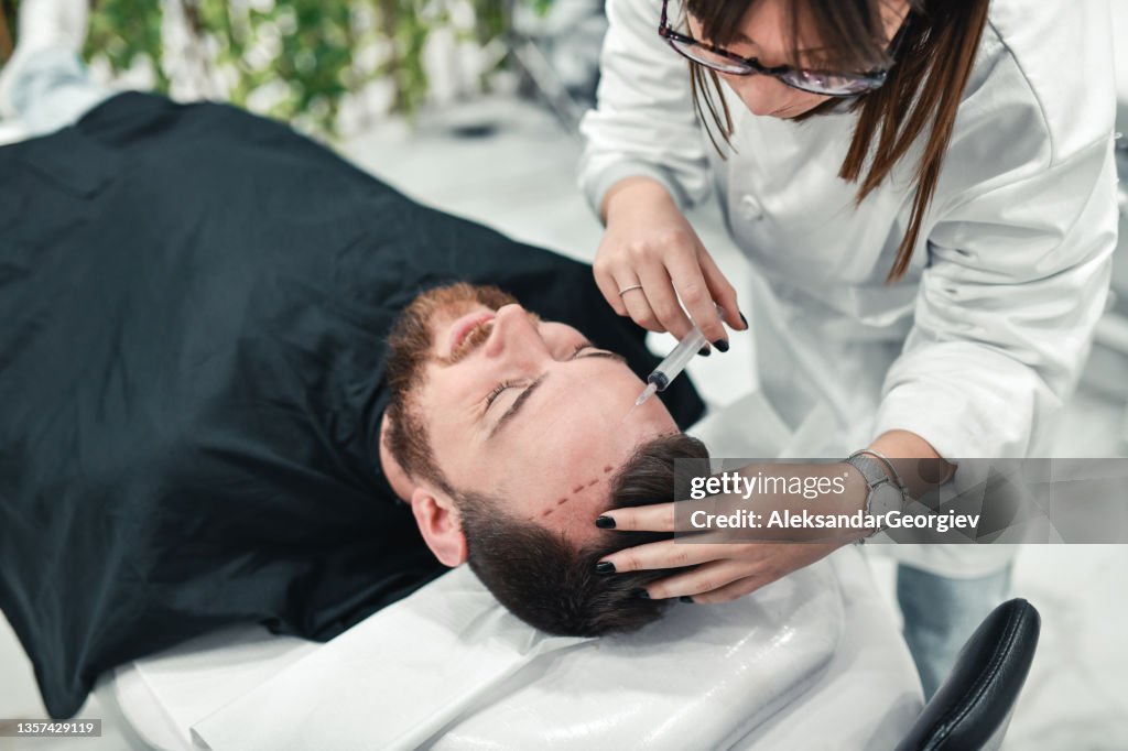 Ärztin bereit, den zurückweichenden Haaransatz des Mannes während der Kahlheitsbehandlung mit Injektion zu stoppen