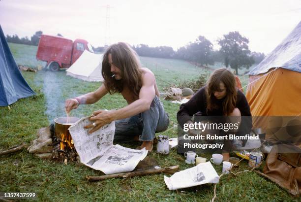 Young man and woman prepare food on a camp fire by their tent at the first Glastonbury Festival, United Kingdom, September 1970.
