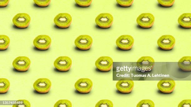 repeated pattern of many sliced ripe kiwi fruits on light green background. - kiwi fruit stock pictures, royalty-free photos & images