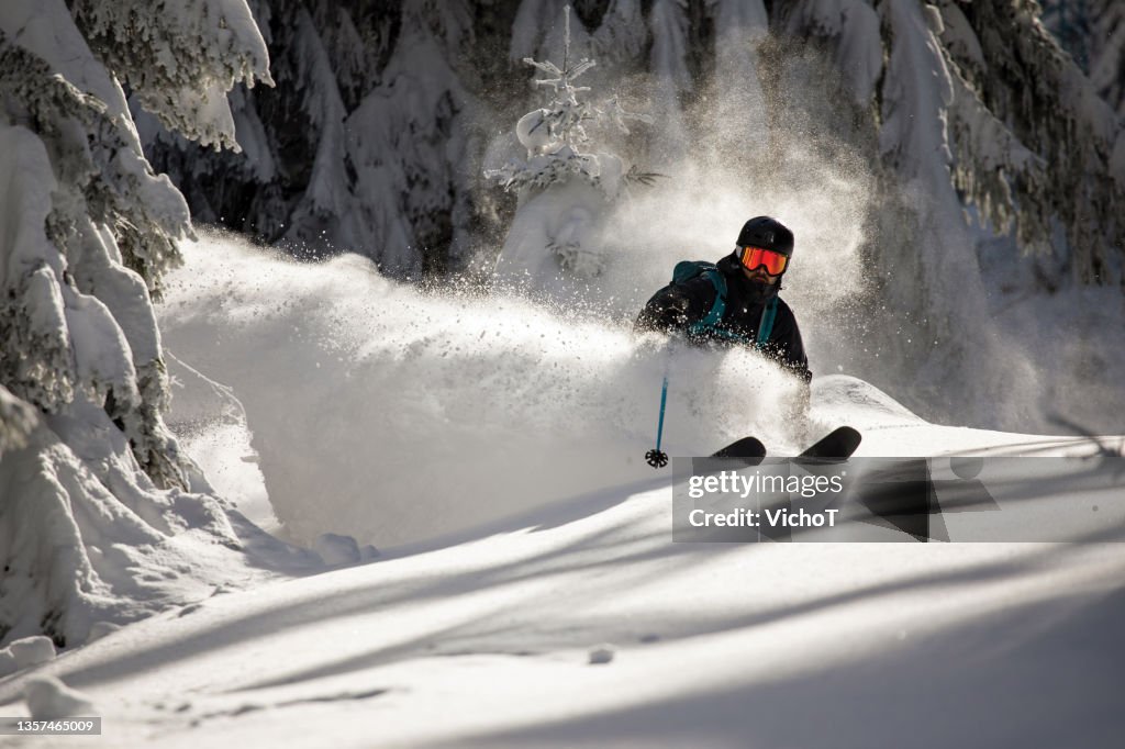 Freeride skier shredding deep fresh powder snow in a winter forest