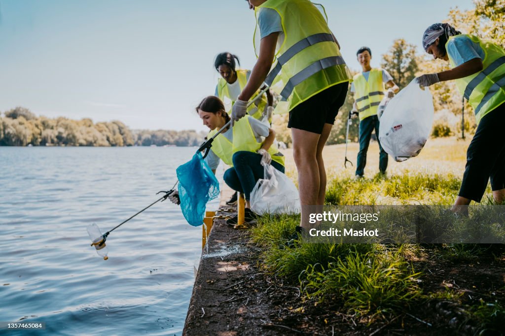 Young female and male environmentalist cleaning lake while picking plastic from claw