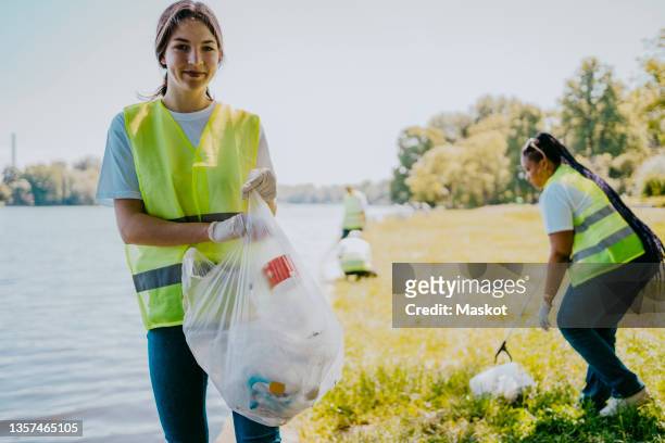 portrait of smiling woman holding plastic bag at lakeshore - activists stock-fotos und bilder