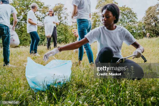 young female environmentalist picking up plastic waste in park - charity day stock-fotos und bilder