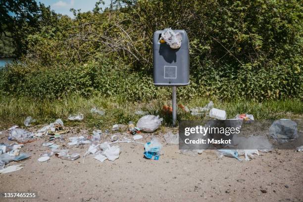 garbage bin littered with plastic wastes around in park - plastikmüll stock-fotos und bilder