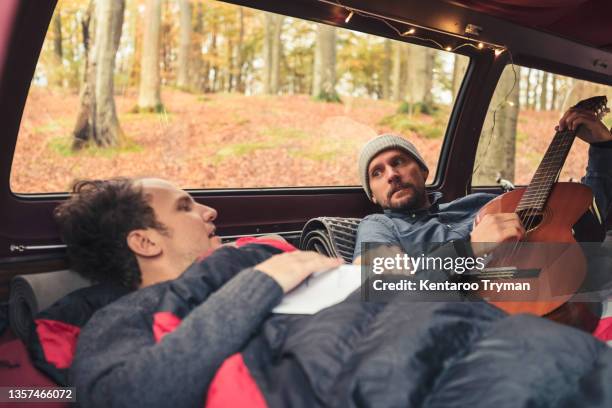 man plucking guitar while lying by male friend in camping van - plucking an instrument - fotografias e filmes do acervo