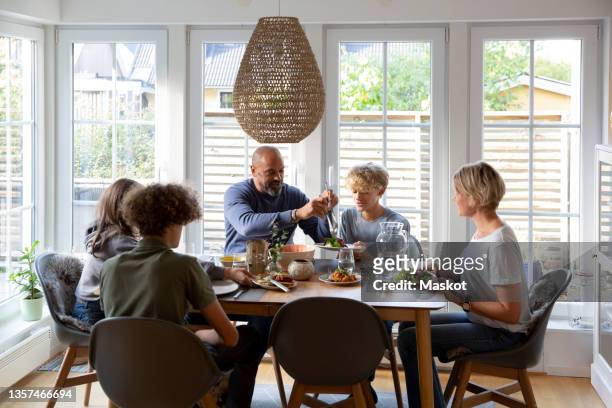 family eating food together at dining table - eettafel stockfoto's en -beelden