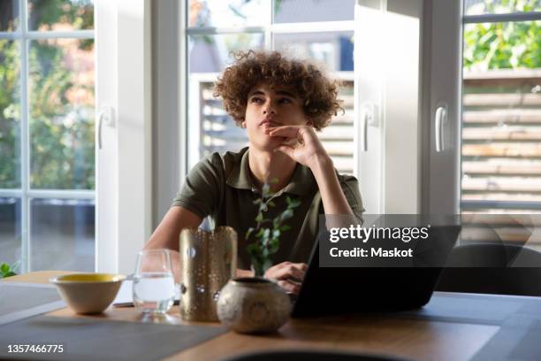 teenage boy contemplating while sitting with laptop at home - boy thinking stock-fotos und bilder