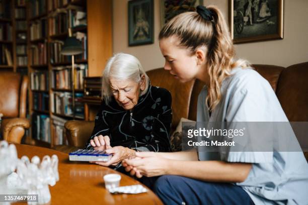 senior woman talking with female caregiver over medicine box in living room - pilulier photos et images de collection