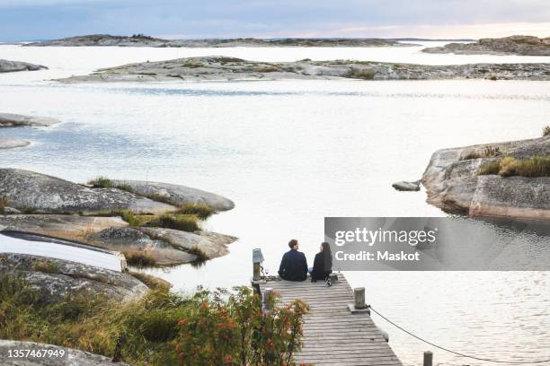 rear view of couple sitting on jetty at sea during summer vacation - stockholm archipelago stock pictures, royalty-free photos & images