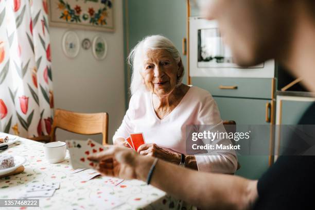 elderly woman playing cards with male nurse at dining table - pflege senioren stock-fotos und bilder