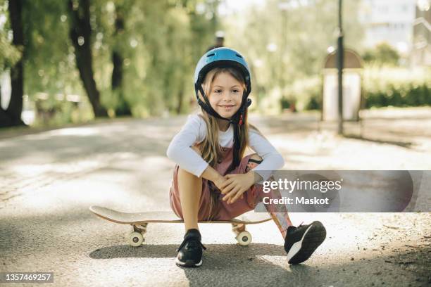 smiling girl with prosthetic leg contemplating while sitting on skateboard - amputado fotografías e imágenes de stock