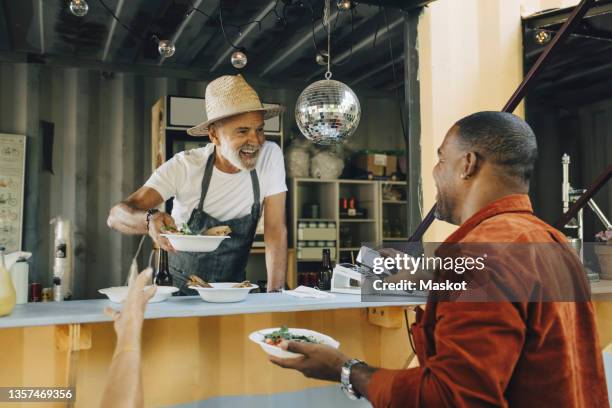 smiling owner serving food while male customer doing contactless payment through smart phone - piccola impresa foto e immagini stock