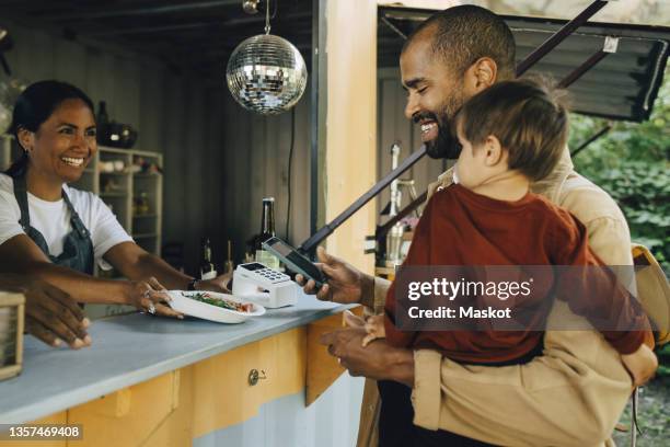 smiling male customer with son doing contactless payment through smart phone - food truck payments stock pictures, royalty-free photos & images