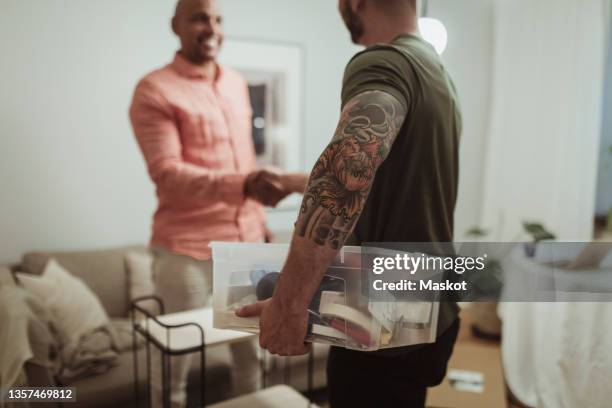 male craftsperson holding toolbox while doing handshake with customer at home - economía colaborativa fotografías e imágenes de stock