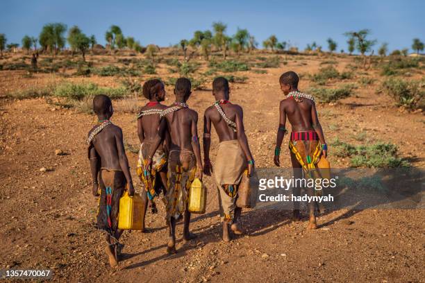 african girls carrying water from the well, ethiopia, africa - hamer tribe stockfoto's en -beelden