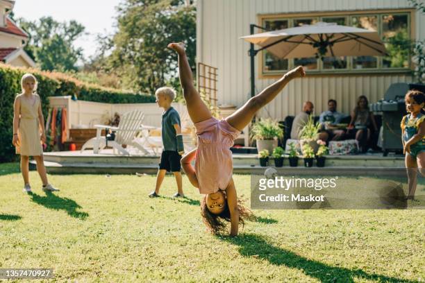 girl doing cartwheel while playing with friends in backyard on sunny day - family backyard stockfoto's en -beelden
