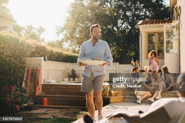 happy man with food walking towards woman during garden party - family backyard imagens e fotografias de stock