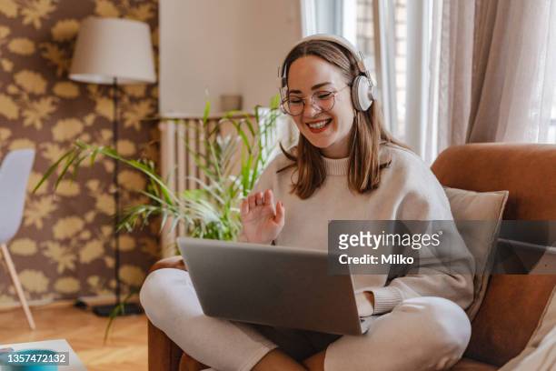 young woman is communicating on video call via laptop in the living room - bank student stockfoto's en -beelden
