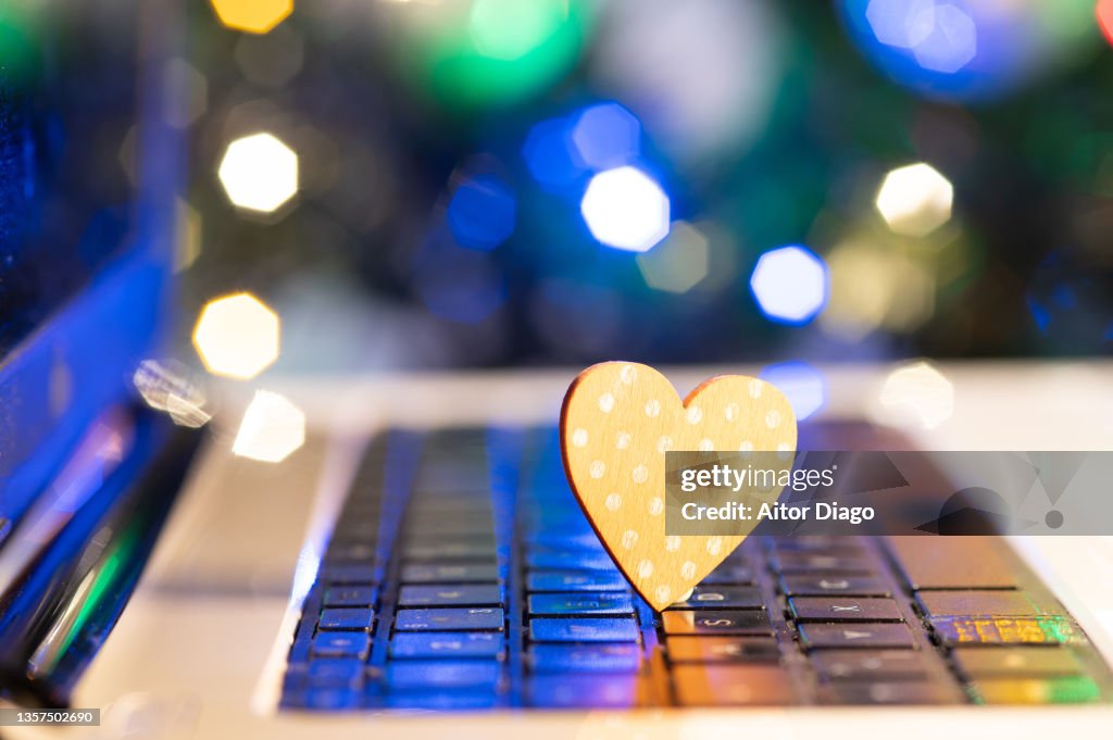 Heart shape on the keyboard of a computer. In the background is a decorated Christmas tree.