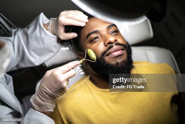 mid adult man receiving a facial massage at a spa - schoonheidsspecialist stockfoto's en -beelden