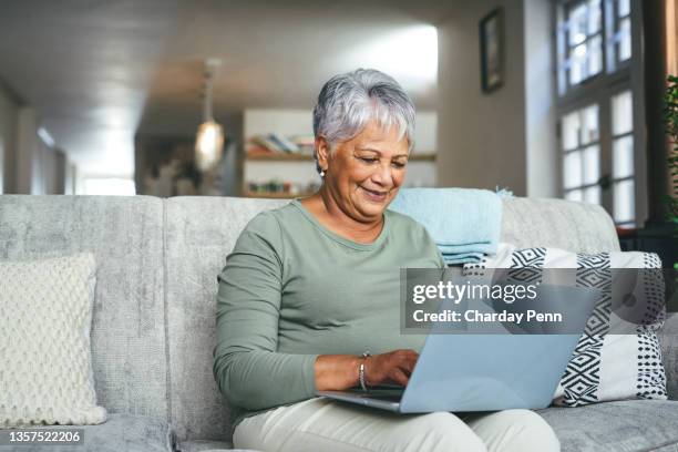 shot of a senior woman using a laptop on the sofa at home - hispanic woman computer stockfoto's en -beelden