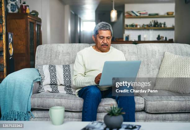 shot of a senior man using a laptop on the sofa at home - senior men computer stock pictures, royalty-free photos & images