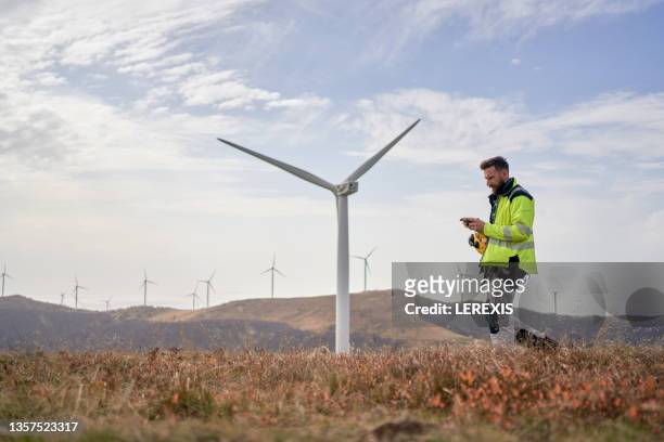 worker with a tablet in his hands against the backdrop of wind turbines - steam turbine stock pictures, royalty-free photos & images