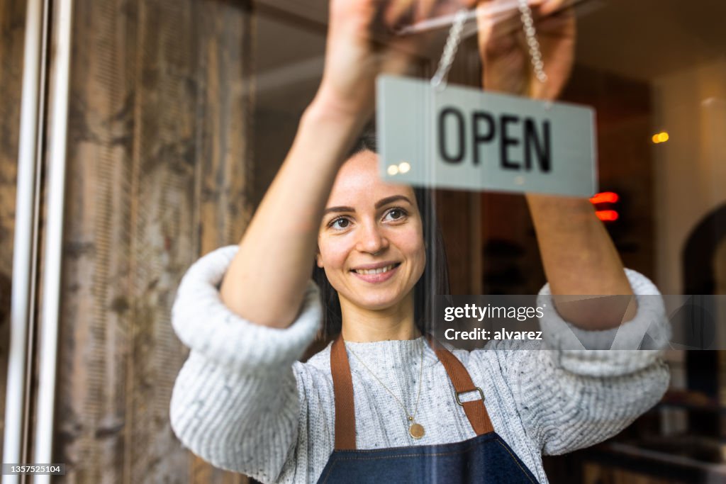 Café-Besitzerin hängt ein offenes Schild in einem Café auf