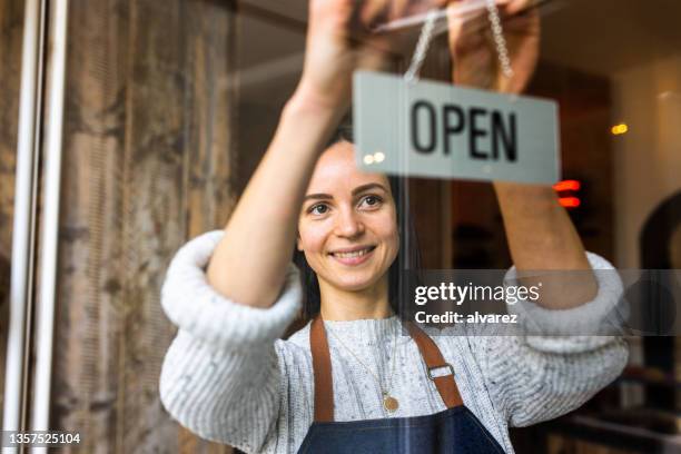 woman coffee shop owner hanging an open sign at a cafe - los stockfoto's en -beelden