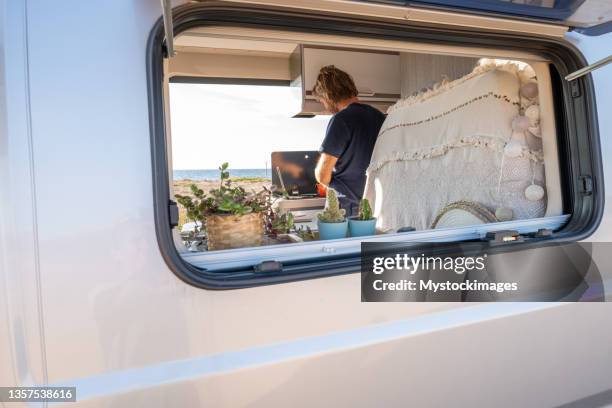 vista della finestra dell'uomo all'interno del furgone che cucina e prepara il cibo, concetto di vita del furgone da campeggio - rv beach foto e immagini stock